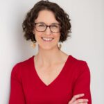 Jennifer Anderson in a red sweater and glasses standing with her arm crossed
