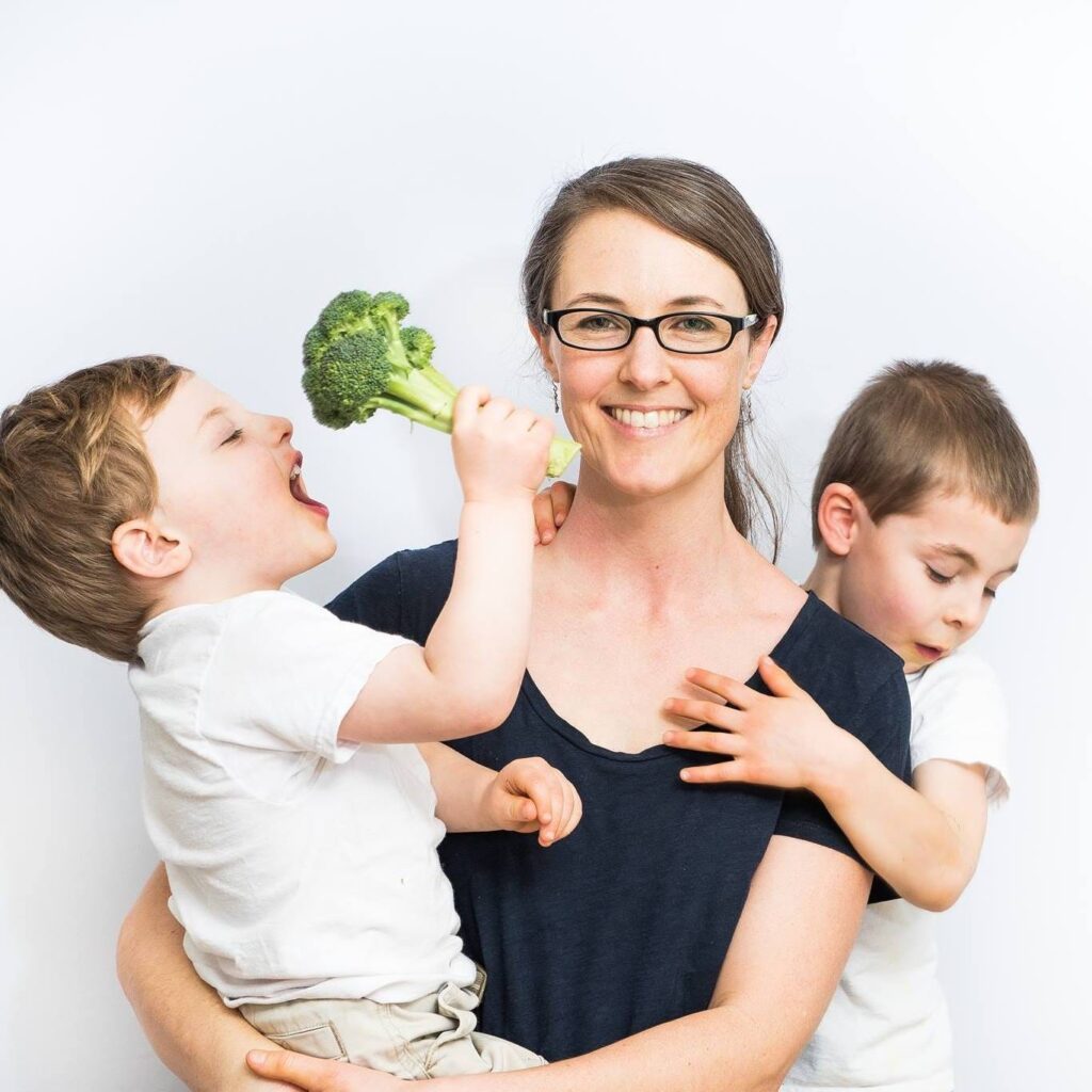 Jennifer Anderson in a navy t shirt and her sons in white t shirts holding broccoli