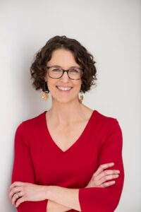 Jennifer Anderson in a red sweater and glasses standing with her arm crossed