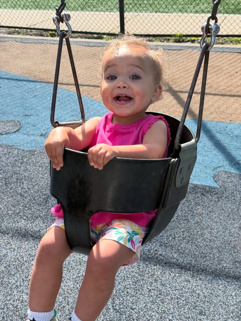 two year old girl in a pink t shirt sitting in an outside swing