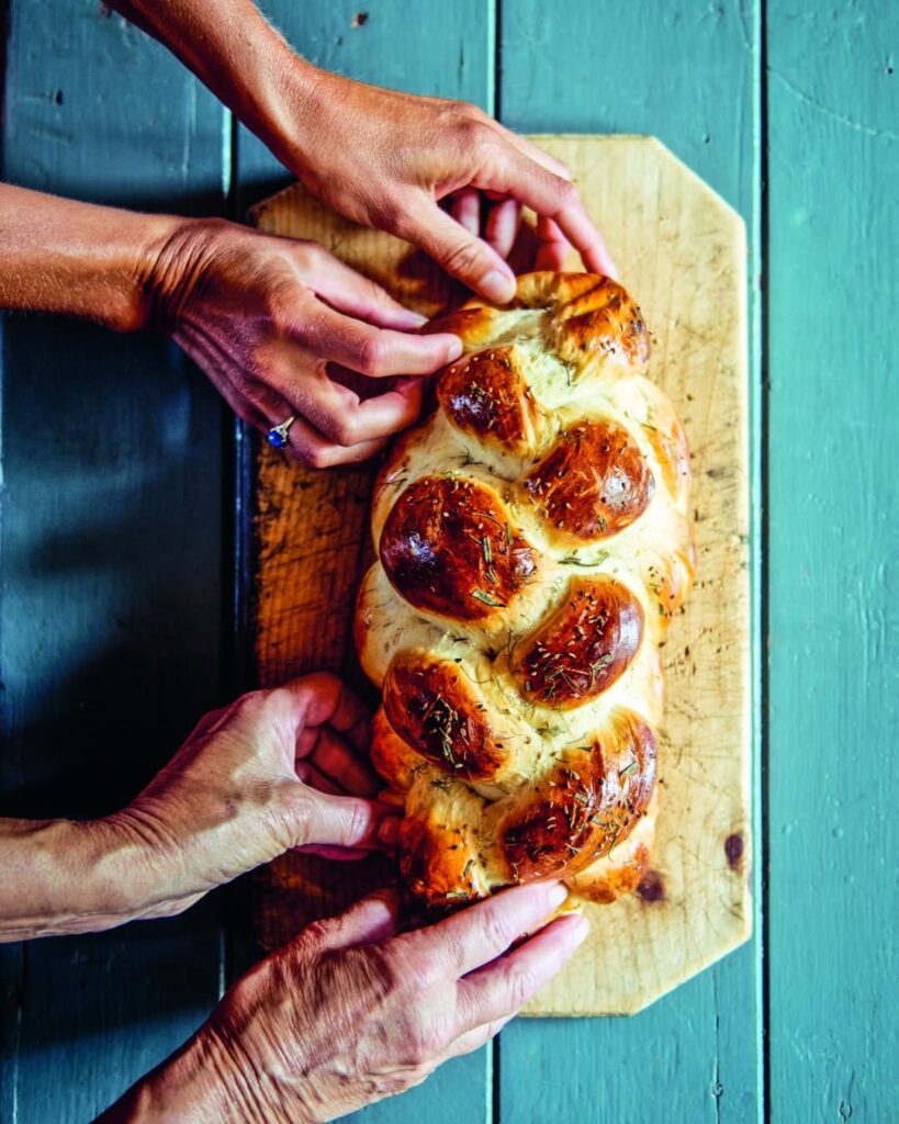 two sets of hands preparing a Challah bread