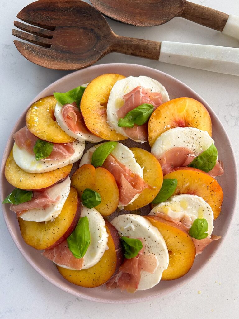 Fresh mozzarella, sliced peaches, and prosciutto with basil laid out in a circle on a serving platter.