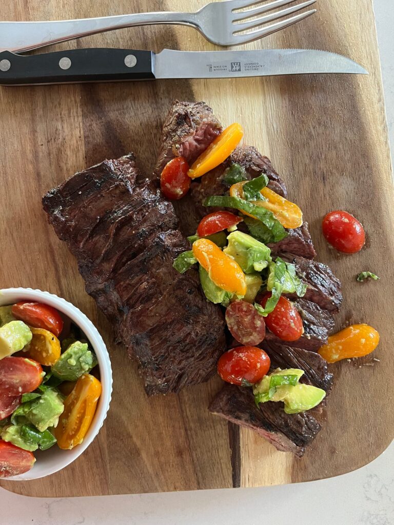 Skirt steak on wooden cutting board with tomato and avocado
