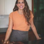 Katie Button in an orange top, smiling in her kitchen