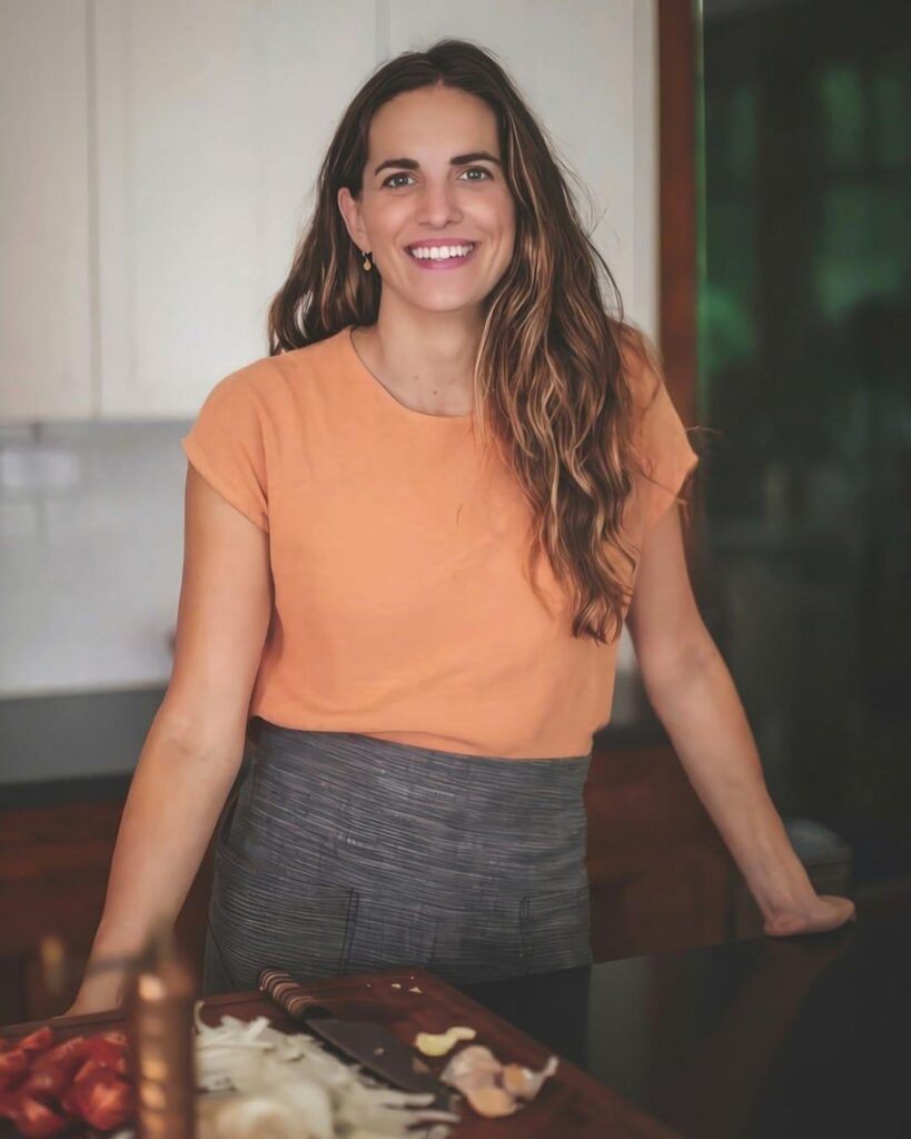 Katie Button in an orange top, smiling in her kitchen