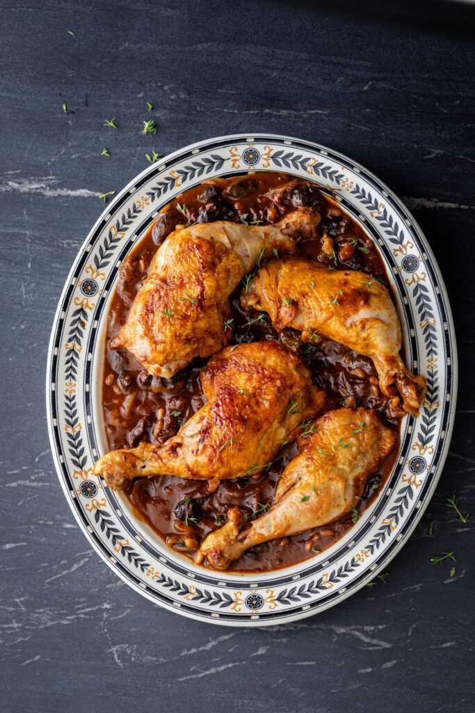 Roast chicken legs in a dark sauce on a patterned oval platter