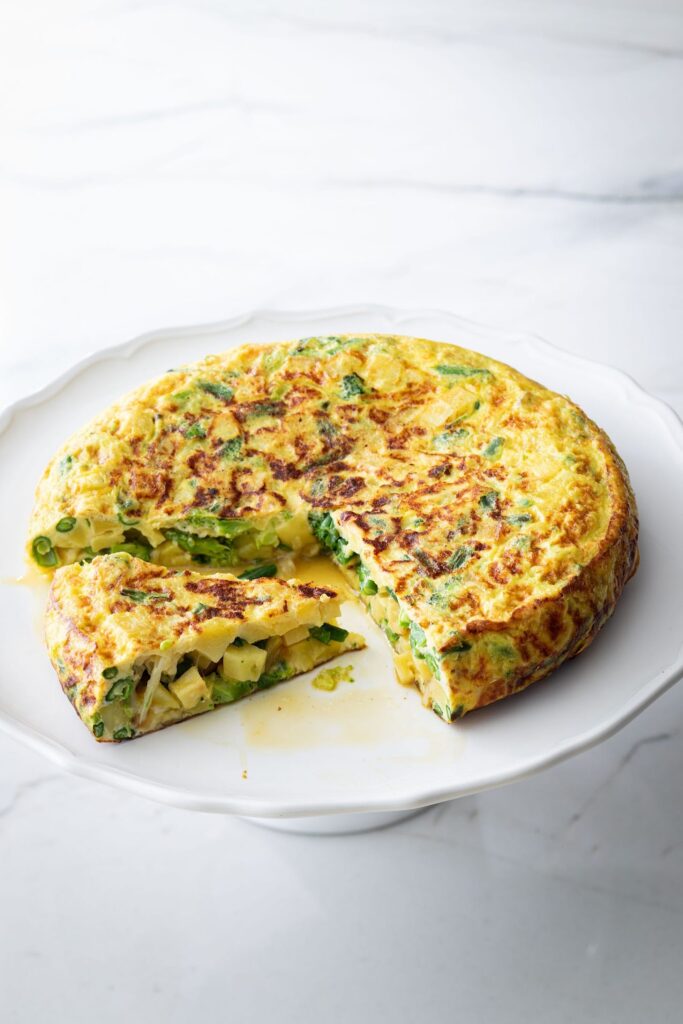 Spanish tortilla with greens, a wedge cut out, on a white cake stand