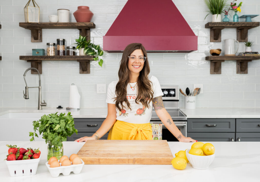 Kris Dovbniak, standing in a kitchen wearing a yellow skirt and white tee shirt