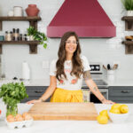 Kris Dovbniak, standing in a kitchen wearing a yellow skirt and white tee shirt