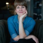 Jewish food writer Leah Koenig author photo, a Caucasian woman seated looking directly at the camera with her hand on her chin.