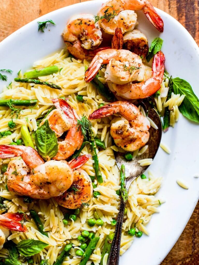 Grilled lemon shrimp with orzo and asparagus salad in a white plate on a wooden table