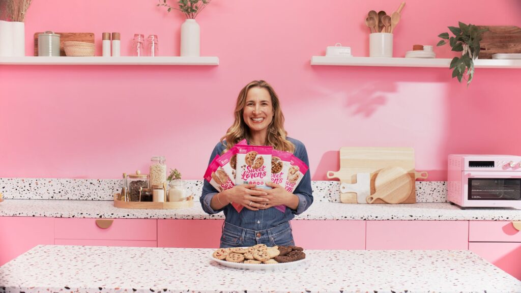 Loren Castle in a pink kitchen holding Sweet Loren's cookie dough packages