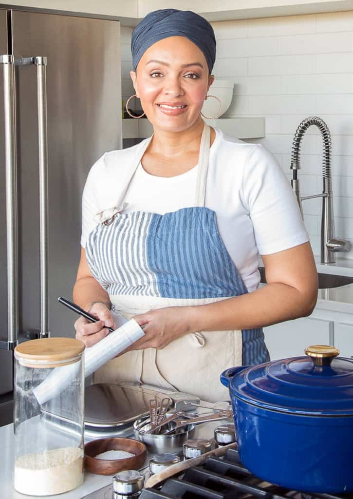 Marta standing at a stove with a notepad and pen in her hand.