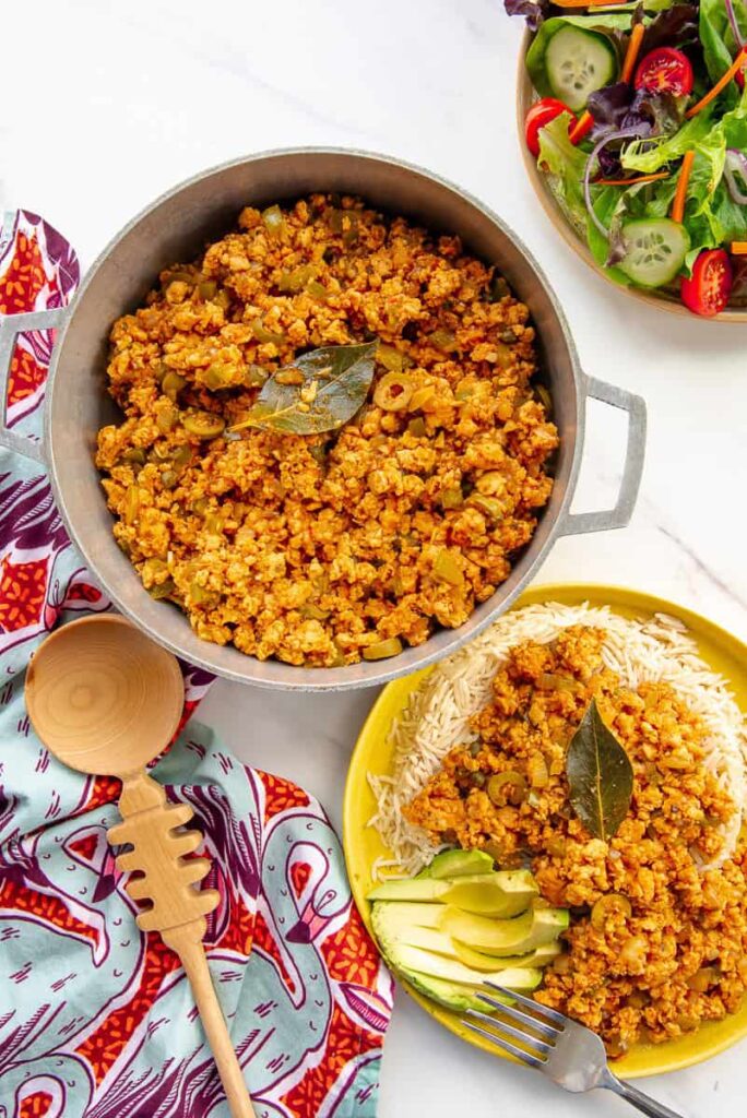 Picadillo de Pavo in a caldero next to a bowl of salad and a serving of turkey picadillo.