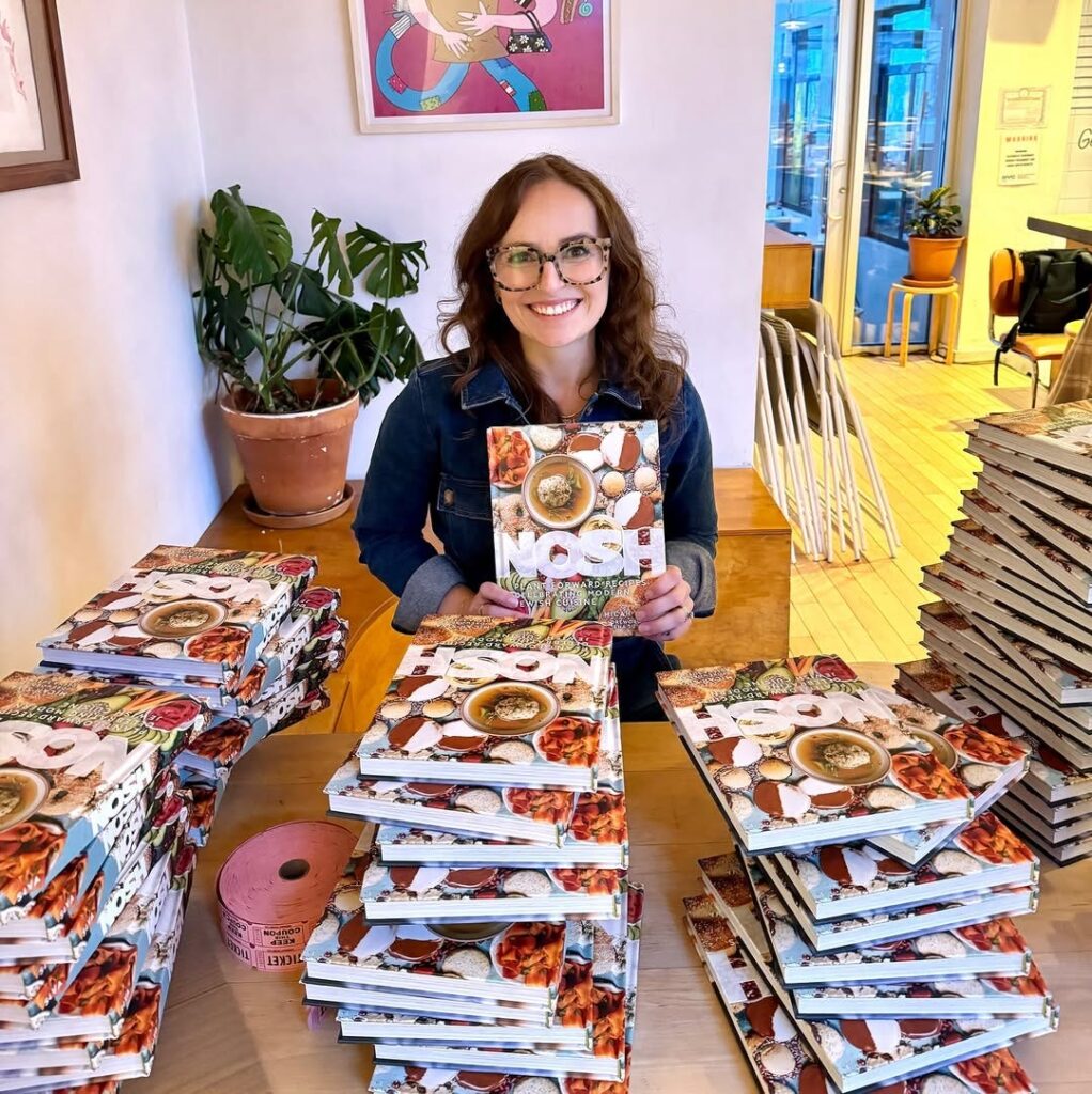 Micah Siva sitting with piles of her cookbook "Nosh" surrounding her