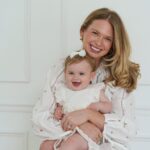 Michelle Schor in a white print dress holding daughter Zoe on her lap