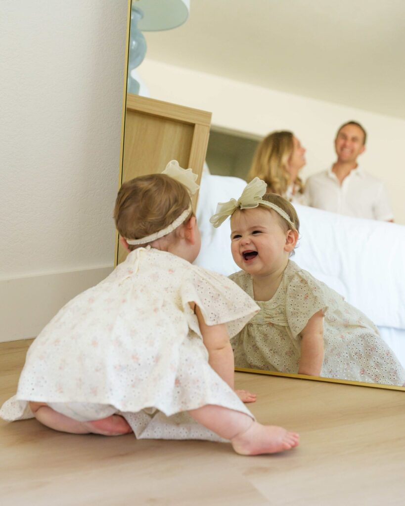Zoe on the bedroom floor smiling into a mirror with Michelle and Aviv in the background