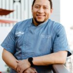 Chef Nelson German in his chef's jacket, leaning on a railing