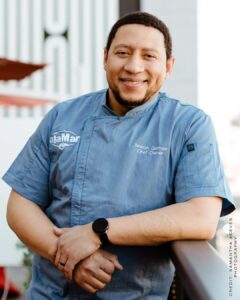 Chef Nelson German in his chef's jacket, leaning on a railing