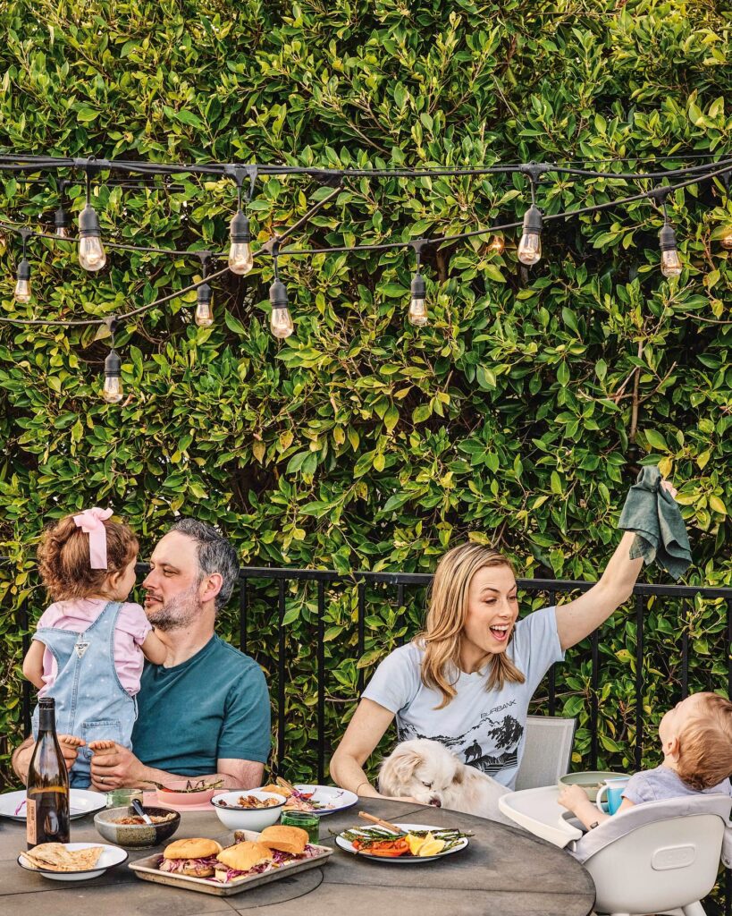 Noah Galuten sitting outside around a round table with plates of food with his wife and two kids