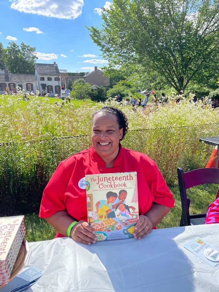 Taffy holding up The Juneteenth Cookbook sitting at a table outside