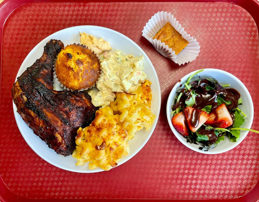 Plate of barbecue chicken, macaroni and cheese, a corn muffin and strawberry salad on a red tray