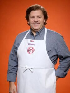 Ted Pappas wear his white chef apron and grey shirt on an orange background